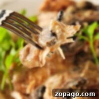 Close-up of a fork holding tender chicken marsala in creamy mushroom sauce, with greens blurred in the background.