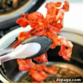 Tongs holding crispy bacon strips showcase the perfection of bacon in the air fryer, a delightful blend of ease and taste.