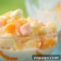 Bowl of creamy, easy ambrosia salad with fruit and pastel marshmallows. Text at the top reads Easy Ambrosia Recipe.