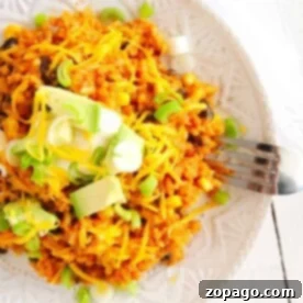 A plate of vibrant instant pot enchilada rice topped with cheese, avocado, and chopped green onions sits invitingly, with a fork ready on the side.