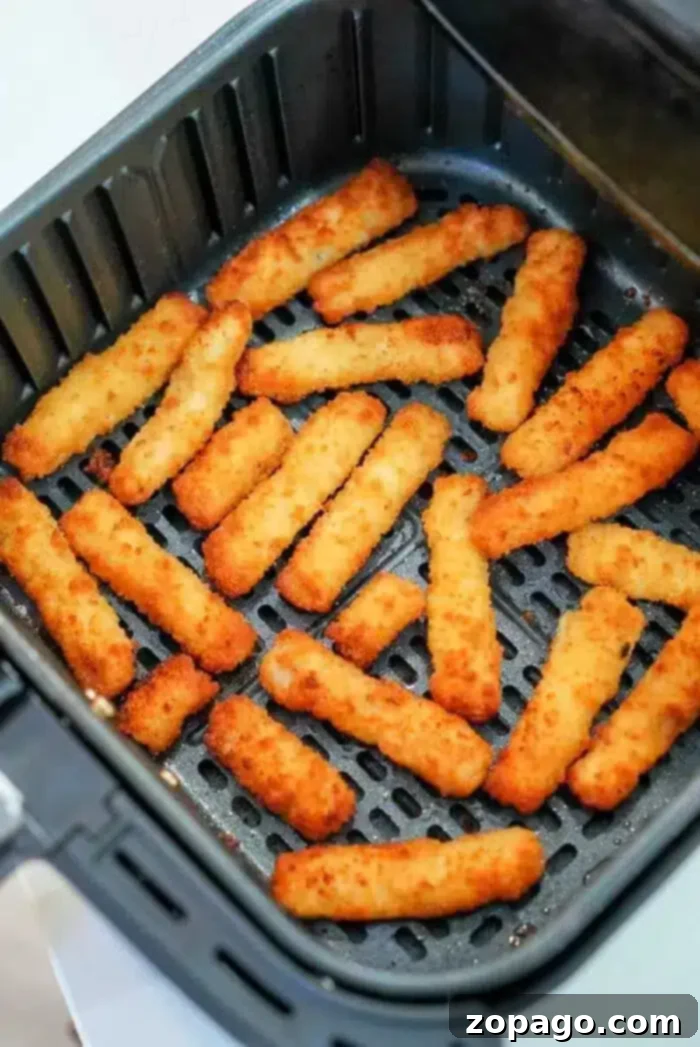 Air fryer fish sticks are the bomb! WAY better than cooking them in your oven, this way you'll get ultra crunchy crispy battered fish in just a few minutes. #airfryerfish #fishsticks #airfryer #airfryerrecipes Several air fryer fish sticks are arranged in a single layer inside an open air fryer basket. The fish sticks are golden brown and appear to be evenly cooked. The air fryer basket is black and has a perforated bottom.