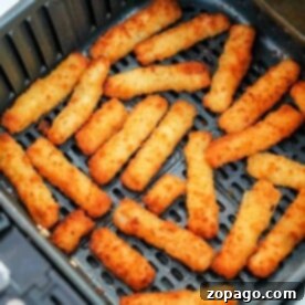 Golden, crispy air fryer fish sticks arranged in a single layer inside an open basket, ready to enjoy.