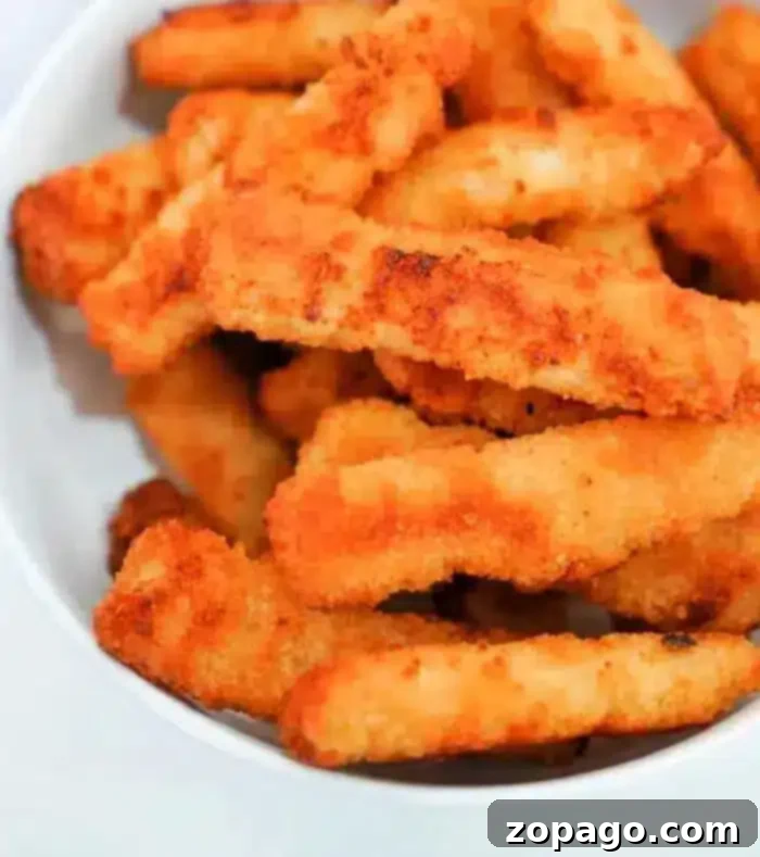 Golden Crispy Air Fryer Fish Sticks 3 A white bowl filled with multiple crispy, golden-brown air fryer fish sticks, arranged in a slightly haphazard manner. The breaded fish sticks appear to be freshly cooked, with a crunchy texture visible. The background is plain and white.