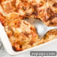 A spoon scoops a delightful fresh peach dump cake from a baking dish on a marble surface.