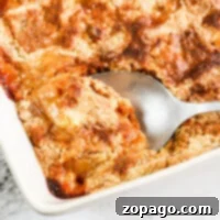 A spoon scoops a delightful fresh peach dump cake from a baking dish on a marble surface.