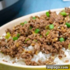 A bowl of fluffy white rice topped with Instant Pot Korean beef and a sprinkle of chopped green onions.