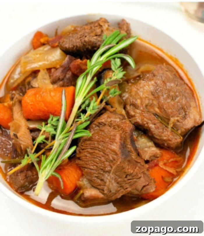 Instant Pot Beef Bourguignon cooked with red wine, vegetables and seasonings turns out amazingly tender and flavorful! A bowl of Instant Pot Beef Bourguignon with large chunks of tender beef, carrots, celery, and onions, garnished with fresh rosemary and thyme in a rich, dark broth.