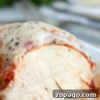 Ultimate Slow Cooker Chicken Parmesan 5 Close-up of a slow cooker chicken parmesan with sliced chicken breast, topped with rich tomato sauce and melted cheese, sprinkled with herbs.