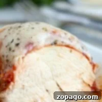 Close-up of a slow cooker chicken parmesan with sliced chicken breast, topped with rich tomato sauce and melted cheese, sprinkled with herbs.