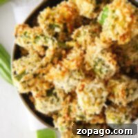 A bowl of crispy, air fryer okra pieces on a white surface, with some fresh okra in the background.