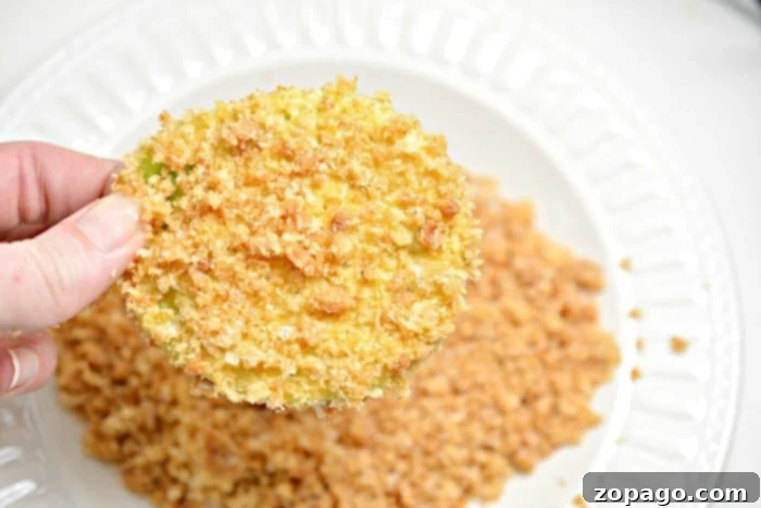 An air fryer basket filled with perfectly breaded green tomato slices, ready for cooking.