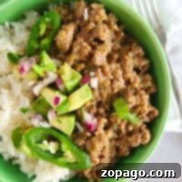 A delicious Instant Pot taco bowl featuring rice, seasoned ground beef, avocado, jalapeños, and onions, with a fork on a light surface.