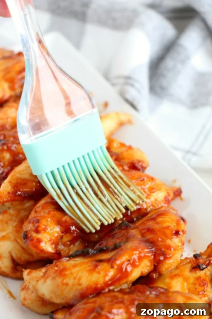Finishing Air Fryer Chicken Tenders with BBQ Sauce A brush applies savory barbecue sauce to freshly air-fried chicken tenders on a white plate, highlighting a delicious no-breading option.