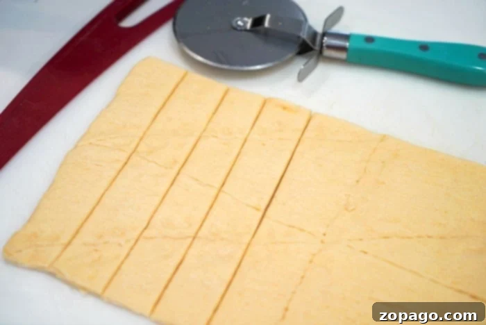 Perfectly Crispy Air Fryer Pigs in a Blanket 5 Rolled-out crescent roll dough sliced into strips with a pizza cutter, ready for wrapping hot dogs.
