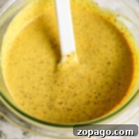 A bowl of creamy mustard pretzel dip sits invitingly, accompanied by a white spatula on a sleek marble surface.