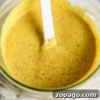 A bowl of creamy mustard pretzel dip sits invitingly, accompanied by a white spatula on a sleek marble surface.