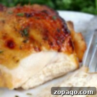 Close-up of marinated chicken breast, perfectly roasted in an air fryer, sliced on a white plate with a fork; herbs in the background.