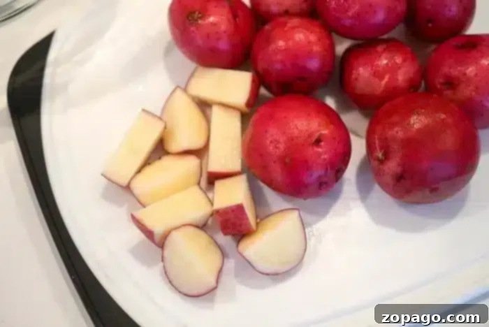 Crispy Air Fryer Red Potatoes 3 Red potatoes are on a cutting board, ready for the air fryer; some are whole while others are cut into chunks. They boast smooth, reddish skin and pale yellow flesh. The white cutting board with a black handle complements this vibrant preparation perfectly.