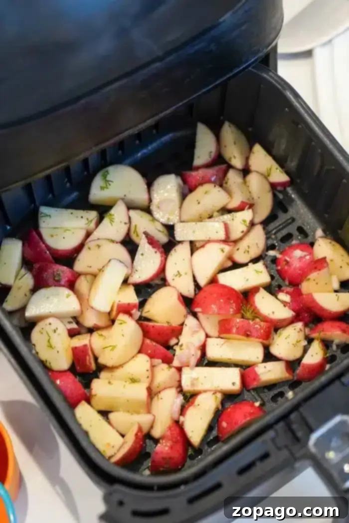 Best air fryer red potatoes with dill and garlic are the best side dish with any dinner. Inexpensive yet full of flavor, you've got to try these tonight. Chopped air fryer red potatoes seasoned with herbs are placed in the basket, ready for cooking.