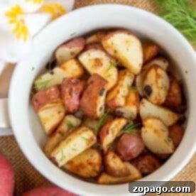 A white bowl filled with air fryer red potatoes, garnished with herbs, surrounded by whole red potatoes.