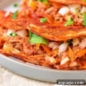 Cheesy tacos filled with succulent crockpot chicken taco meat, chopped onions, and cilantro on a white plate.