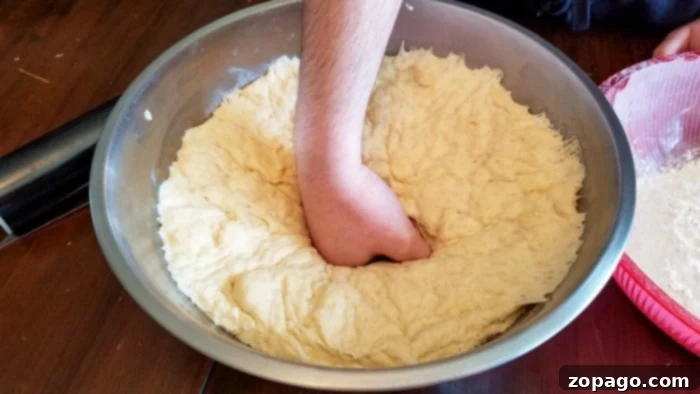 Cloud-Like Homemade White Bread 5 A hand gently punching down risen white bread dough on a floured surface to release air.