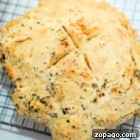 A round loaf of golden-brown bread with herb flecks, cooling on a wire rack, showcases how to make bread with no yeast, delivering a delightful aroma and rustic charm.