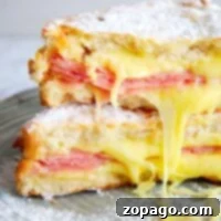 An Air Fryer Monte Cristo Sandwich, stacked with ham and cheese, is perfectly dusted with powdered sugar and served on a plate.
