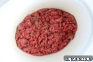 A white slow cooker holds raw ground beef, ready to be transformed into a hearty crockpot meal.