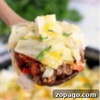 A close-up of a spoonful of unstuffed cabbage roll casserole reveals layers of cooked cabbage, ground meat, diced tomatoes, and melted cheese. Fresh herbs garnish the top. In the background, more casserole awaits in the pan.