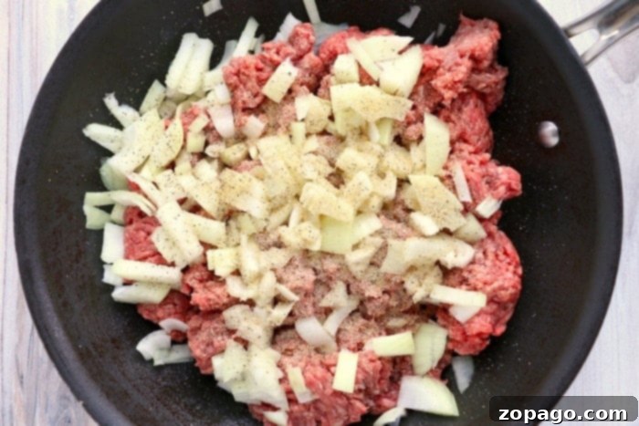 Cottage Pie 3 Chopped onions and ground beef sizzling in a black frying pan, seasoned with pepper and ready for gravy.