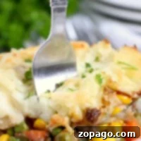Cottage Pie 5 Close-up of a fork in a plate of Shepherd's Pie with ground beef, surrounded by vibrant vegetables and creamy mashed potatoes.