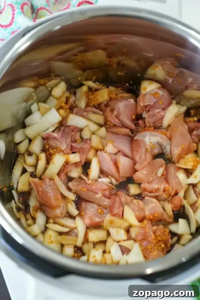 Effortless Instant Pot Korean Chicken 5 A metal pot contains uncooked diced chicken, chopped onions, and minced garlic. The ingredients are in the process of being sautéed, with some onions already starting to turn translucent, creating the base for a delicious Instant Pot Korean chicken dish.