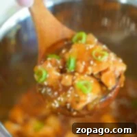 A wooden spoon holding delicious Korean chicken, topped with green onions and sesame seeds, hovers above an Instant Pot.