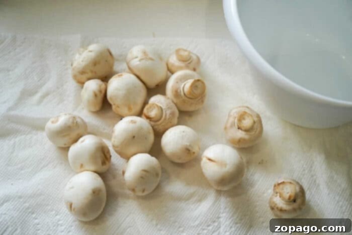 Crispy Air Fried Mushrooms 4 White mushrooms, perfect for air fryer mushrooms, scattered on a paper towel next to a white bowl.