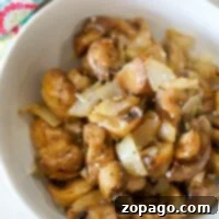 A bowl of air fryer mushrooms with onions, topped with spices, sits next to a colorful patterned towel.