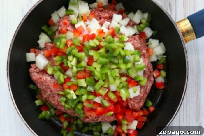 Crispy Air Fryer Empanadas 5 Ground meat with chopped onions, red and green bell peppers sizzling in a black frying pan, ready for empanada filling.