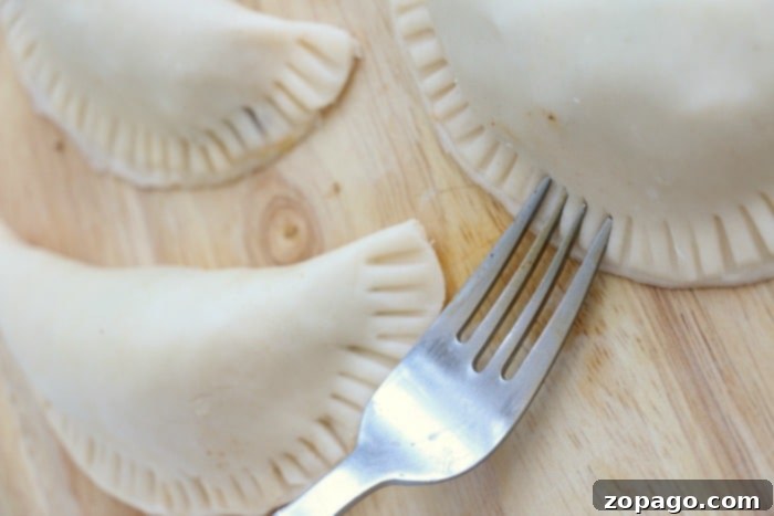 Crispy Air Fryer Empanadas 6 Three uncooked air fryer empanadas resting on a wooden surface, with fork-pressed edges sealing the filling.