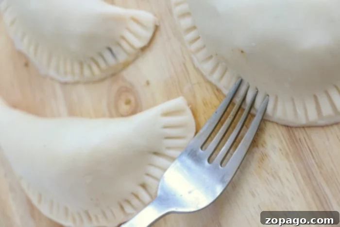 Crispy Air Fryer Empanadas 6 Three unbaked empanadas on a wooden surface, showing the fork-pressed edges ready for air frying.