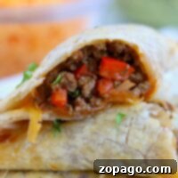 A close-up of two air fryer empanadas, one cut open to reveal a filling of ground meat and chopped red peppers, garnished with herbs.