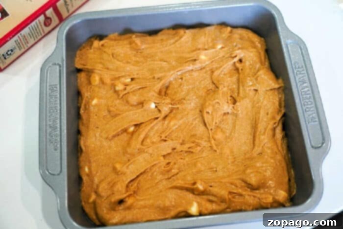 Golden Harvest Pumpkin Blondies 4 Baking pan filled with smooth, unbaked pumpkin blondies batter, studded with white chocolate chips, eagerly awaiting its turn in the oven.