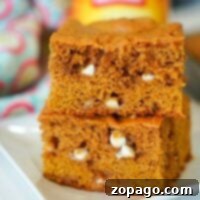 A pair of pumpkin blondies, brimming with white chocolate chips, is temptingly stacked on a plate.