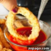A hand dipping a golden-brown, air fryer calamari ring into a bowl of red sauce.