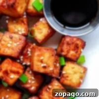 Golden brown tofu cubes, perfectly crisped in the air fryer, sprinkled with sesame seeds and green onions, served with a small dish of dark soy sauce.