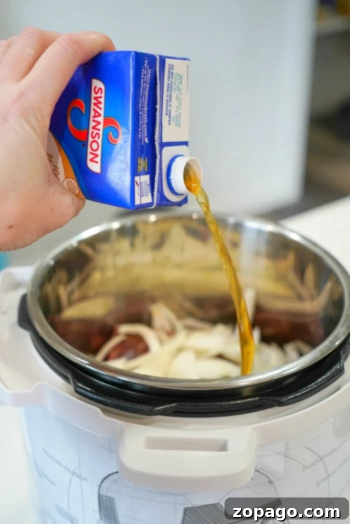 Tender Instant Pot BBQ Beef 6 Pouring broth from a carton into a pressure cooker with sliced onions inside, preparing the base for a savory Instant Pot BBQ beef dish.