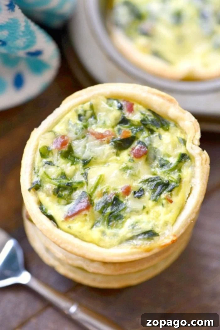No-Fuss Spinach Quiche 6 Close-up of an easy mini quiche with spinach and bacon on a wooden table, fork at the ready, showcasing a simple yet delicious recipe.