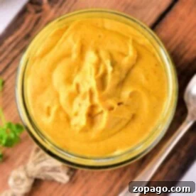 A jar of creamy yellow mustard sauce for corned beef sits on a wooden board, accompanied by a spoon and a twine decoration nearby.