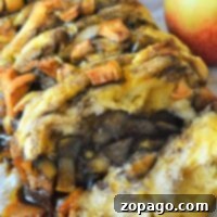 A close-up of a baked cinnamon pull-apart bread rests on parchment paper, with a fresh apple beside it, highlighting the warm and inviting aroma.