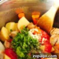 A pot filled with chopped vegetables, herbs, and chunks of pork stew is being stirred with a wooden spoon in an instant pot.