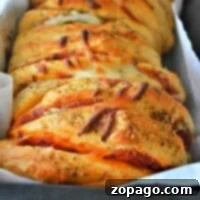 A close-up of freshly baked pull apart pizza bread slices, seasoned with herbs in a tray.